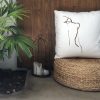 figura white cushion made of 100% cotton, with print design of female figure’s back on a wicker stool outdoors.