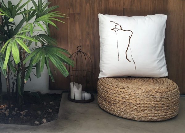 figura white cushion made of 100% cotton, with print design of female figure’s back on a wicker stool outdoors.