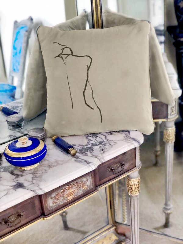 figura beige cushion made of 100% cotton, with print design of female figure’s back on a marble table with back mirror.