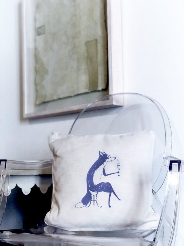 foxy white cushion made of 100% cotton, with a wonderful print of a blue fox drinking wine on a transparent plexiglass chair in a living room.