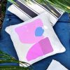 lara pink Linen white garden cushion 46x46 with geometric patterns in pink tones outdoors on grass along with other cushions and palm trees.