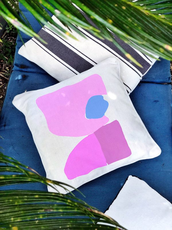 lara pink Linen white garden cushion 46x46 with geometric patterns in pink tones outdoors on grass along with other cushions and palm trees.