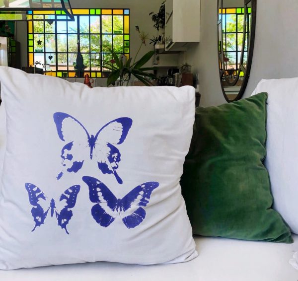 madeleines Λινό λευκό μαξιλάρι κήπου 46x46 με μπλε πεταλούδες πάνω σε λευκό καναπέ σπιτιού