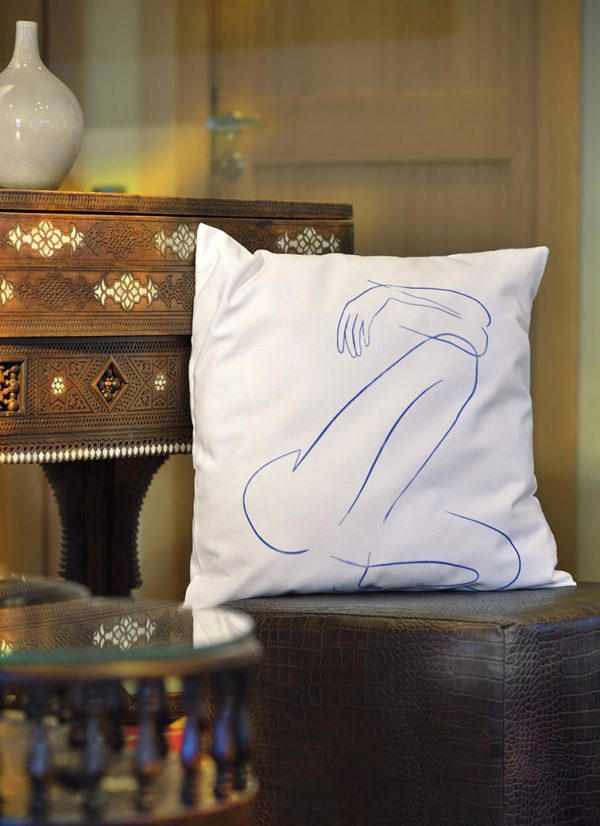 blue fabula white cushion made of 100% cotton, with print design of female body, on a leather stool decorates interior.