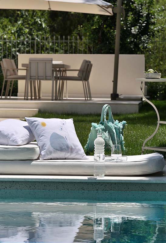 Fiorre di Roccia Λευκό μαξιλάρι από 100% βαμβάκι, και σχέδιο λουλούδι σε μπλέ βράχο σε κήπο μπροστά από πισίνα.