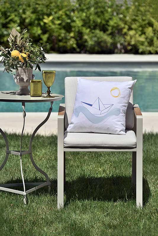 sailing Λευκό μαξιλάρι από 100% βαμβάκι, και σχέδιο μπλε καραβάκι και ήλιο πάνω σε καρέκλα κήπου μπροστά από πισίνα.