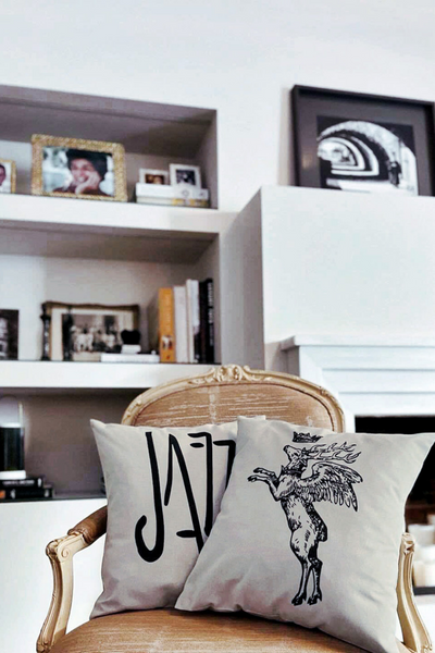 Τετράγωνα μπεζ διακοσμητικά μαξιλάρια με μαύρο τύπωμα ζώου τάρανδου και της λέξης jazz μουσική, τοποθετημένα σε vintage πολυθρόνα σαλονιού