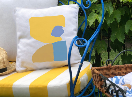 Τετράγωνο λευκό διακοσμητικό μαξιλάρι με κίτρινα και γαλάζια αφηρημένα σχέδια, τοποθετημένο σε κλασικό μπλε μεταλλικό κλασικό καναπεδάκι κήπου