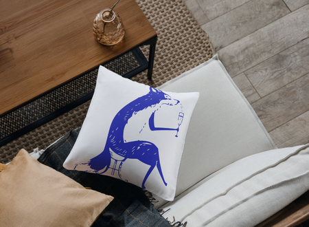 Άσπρο τετράγωνο διακοσμητικό μαξιλάρι με σχέδιο μίας μπλε αλεπούς που πίνει κρασί τοποθετημένο σε καναπέ δίπλα σε ξύλινο τραπέζι