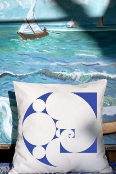 Λευκό διακοσμητικό μαξιλάρι με σχέδιο μπλε κοχύλι τοποθετημένο μπροστά από ένα πίνακα ζωγραφικής με θέμα θάλασσα με κύματα και βάρκες
