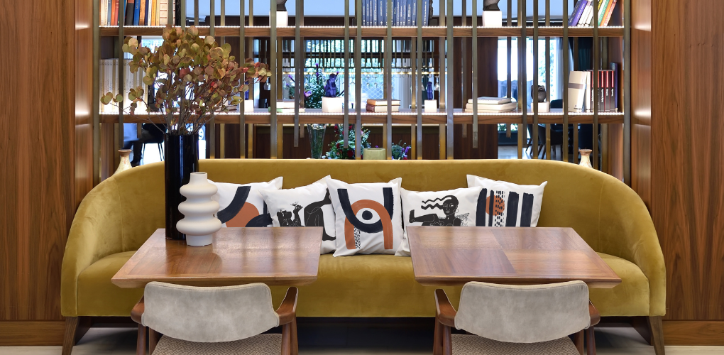 Τετράγωνα λευκά διακοσμητικά μαξιλάρια με τυπώματα σε καφέ και μαύρα χρώματα και σχέδια από έργα τέχνης καλλιτεχνών από όλο τον κόσμο, τοποθετημένα σε καναπέ εστιατορίου, ξενοδοχείου ή μπαρ
